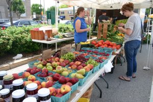 Fresh produce including pears, grapes, peaches, tomatoes, and berries on tables at an outside market.