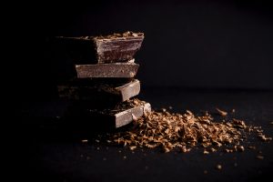 Stacked square pieces of a dark chocolate bar with dark chocolate shavings.