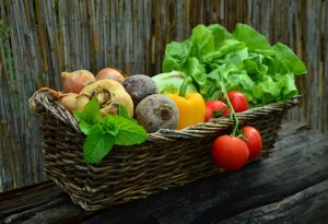 A basket of vegetables and greens, including onions, tomatoes, bell peppers, beets, fresh herbs, and lettuce.