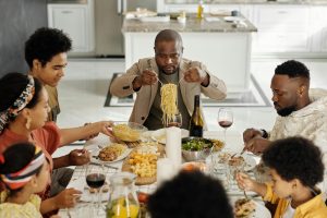 Three Black adults and 4 children enjoying a family-style meal of noodles, meat, salad, and cheese cubes.