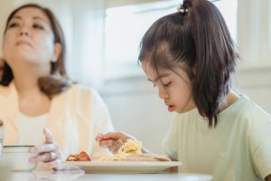 A girl with Down syndrome eats breakfast next to her mother.