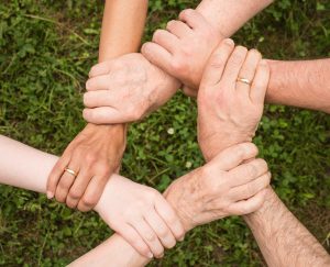 Six multicultural men and women form a circle by holding each other’s wrists.