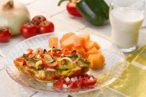 The baked egg dish is topped with onions and thin strips of red and green peppers. The salsa includes sliced cherry tomatoes, garlic, and diced onion.