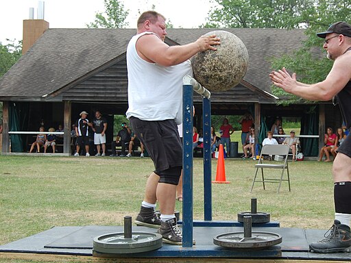 A strongman lifting a heavy round stone over a bar