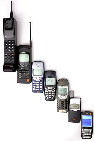 A photo of earlier versions of mobile phones in a series, growing smaller, cascading down from left to right, with a plain white background.