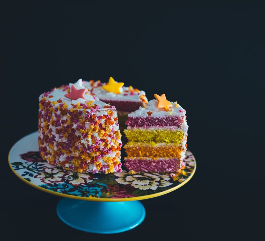 Colorful birthday cake on a cake stand with a slice of cut out